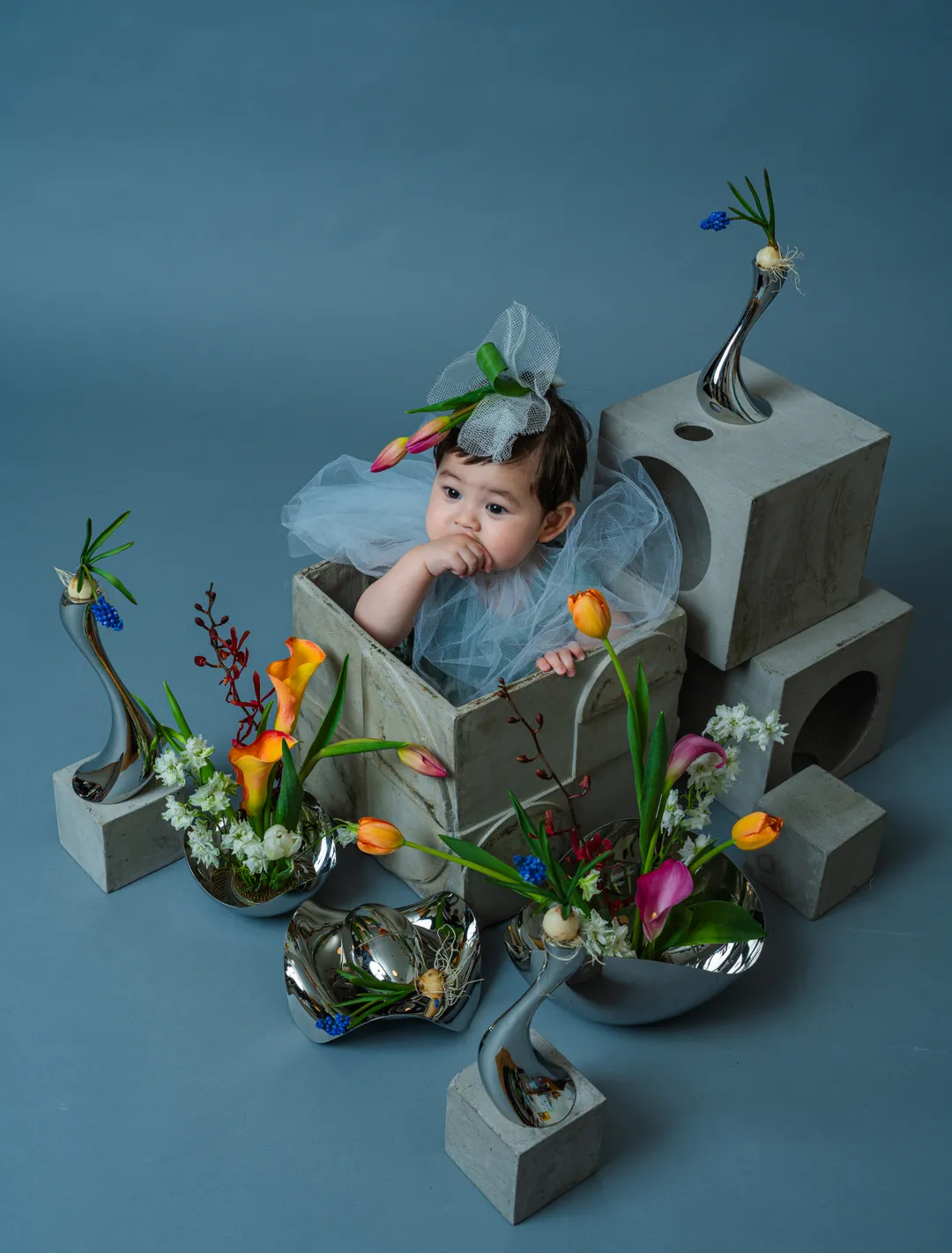 コンクリートブロックと銀の花器・生花に囲まれて箱に入る赤ちゃんのスタジオ作品
