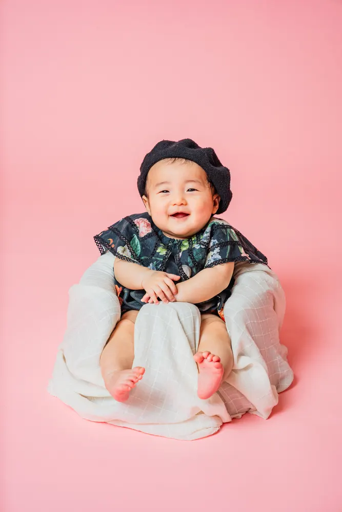 ベレー帽をかぶってちょこんと座る笑顔の赤ちゃん