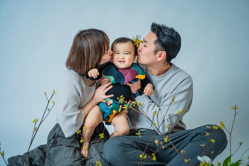 ベージュの服でそろえた両親が子どもの頬にキスをする家族写真(白リンクコーデ例)