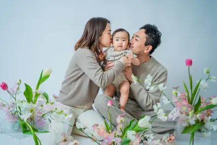 チューリップや白い花に囲まれ赤ちゃんの両頬に両親がキスをする家族3人