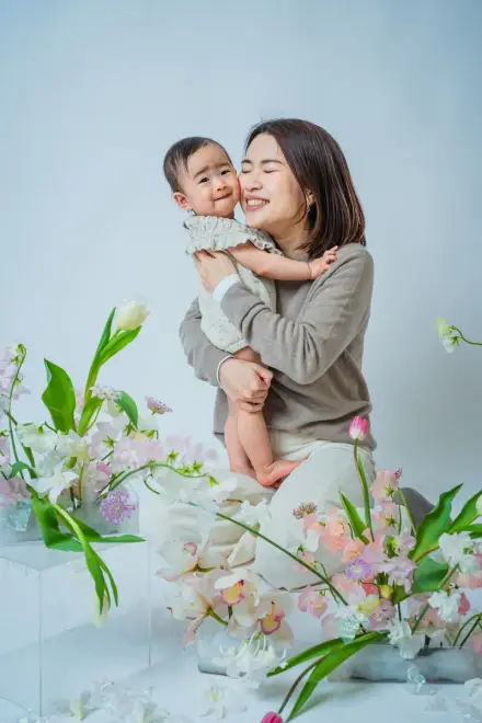 春のチューリップと白い花に囲まれて目を細めながら赤ちゃんをぎゅっと抱きしめる人物