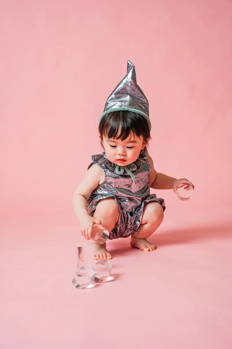 ピンク背景でシルバーの衣装と帽子を身につけて遊ぶ赤ちゃん
