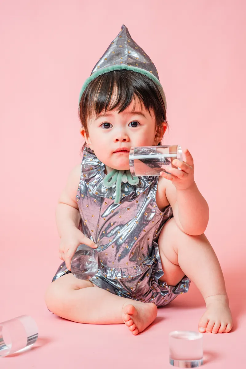 シルバーの衣装と帽子でグラスを手にする赤ちゃん