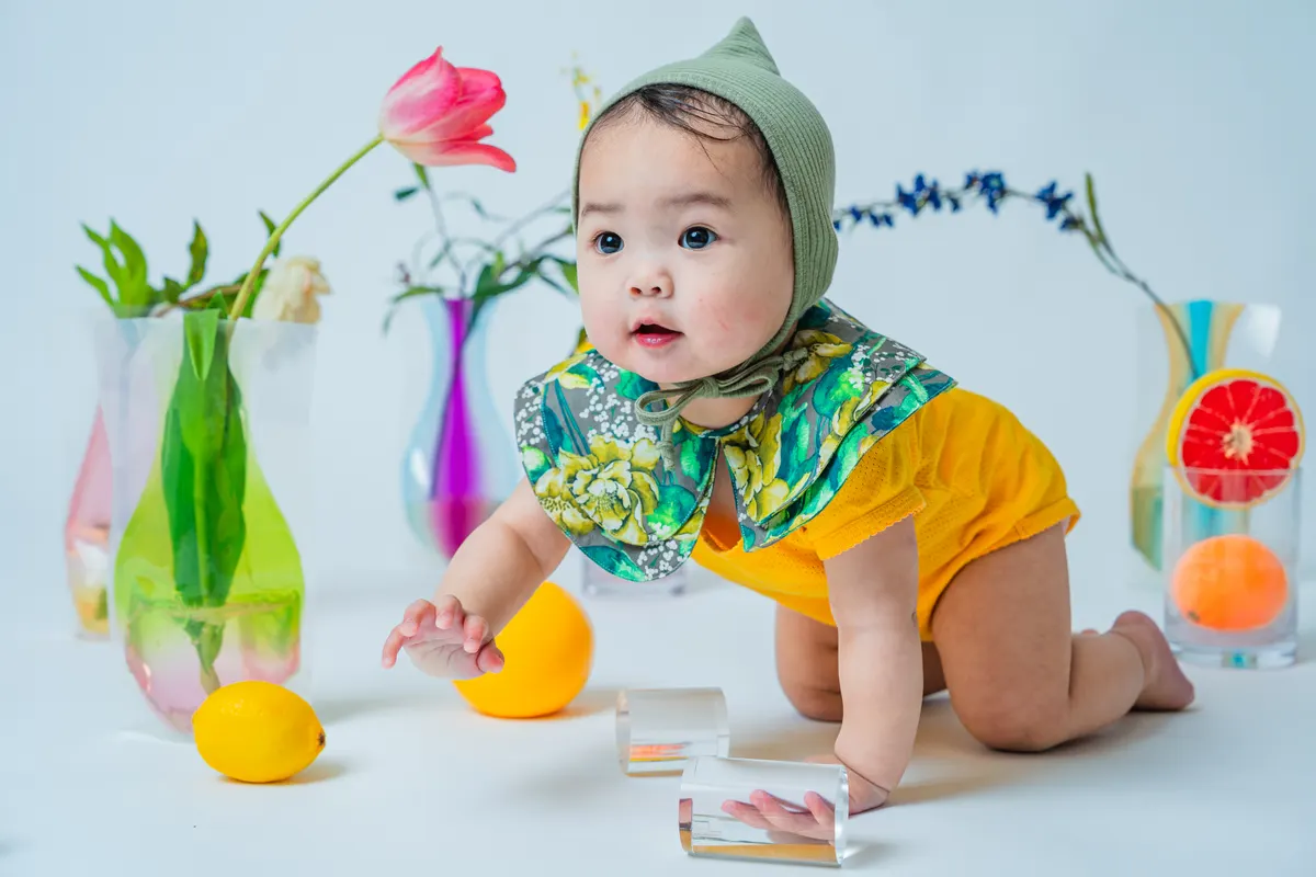 柑橘の果物と花に囲まれてハイハイする黄色い衣装の赤ちゃん（Fruit シーン）