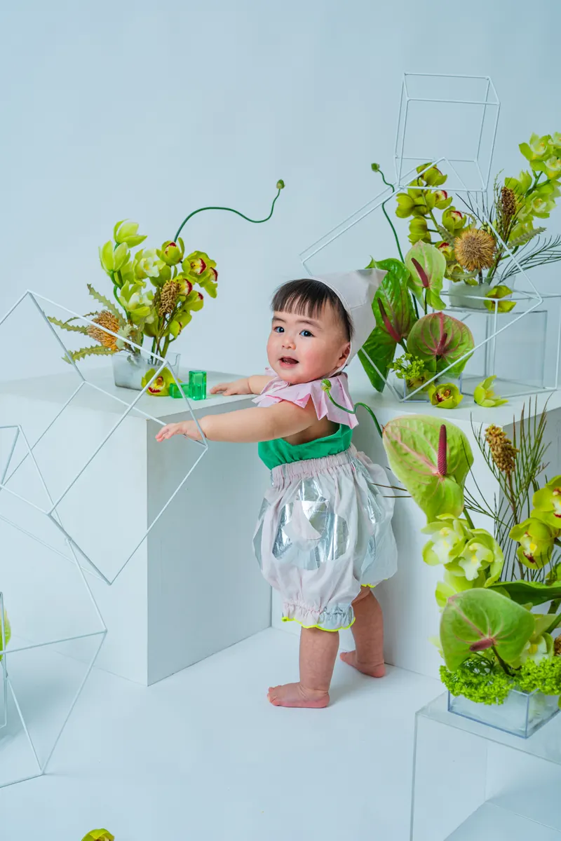 緑の花のセットに手をかけて笑う赤ちゃん（Garden シーン）