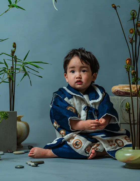 濃紺に車紋などの宝づくし柄の着物「紺」を着て座る男の子