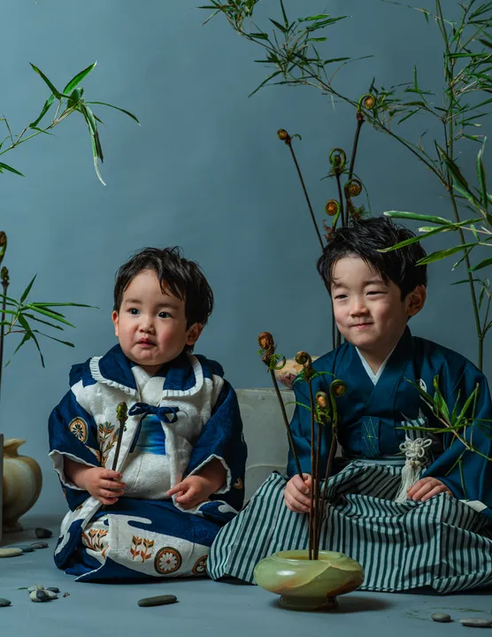 濃紺に車紋などの宝づくし柄の着物「紺」を着て並んで座る子ども