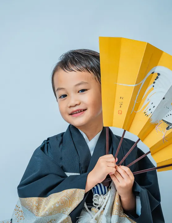 黒地に兜や宝船柄の羽織に縞袴を合わせた着物「鷹」を着た男の子