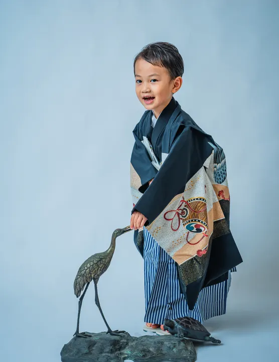 黒地に兜や宝船柄の羽織に縞袴を合わせた着物「鷹」を着た男の子