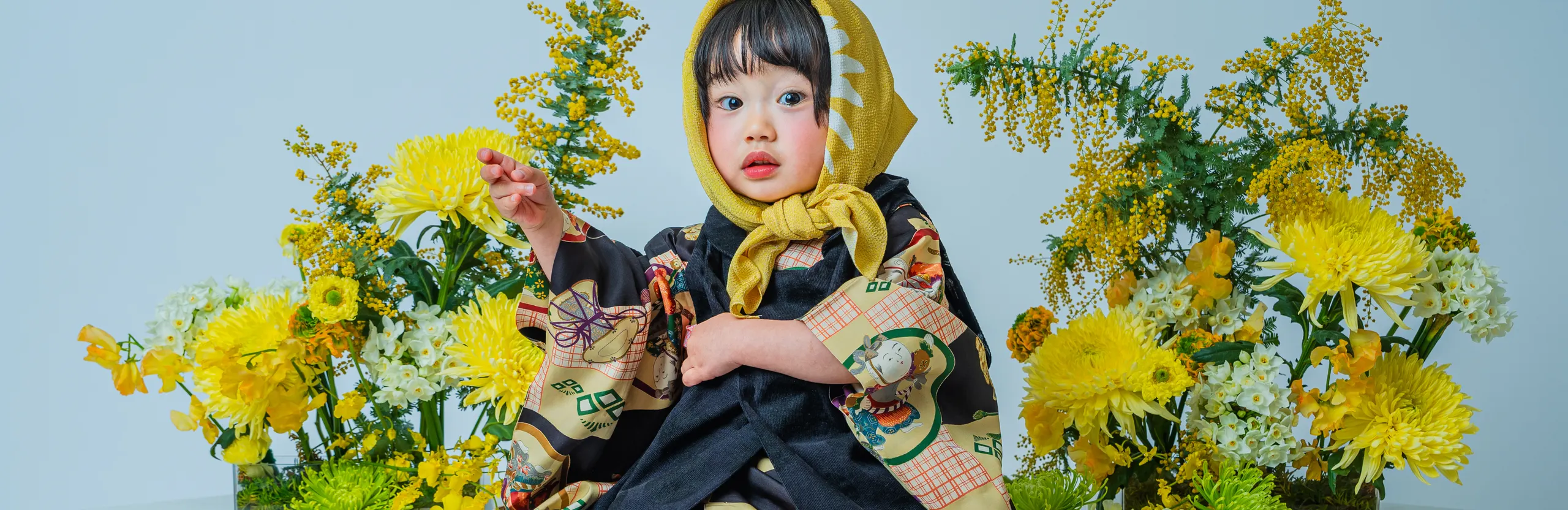 黄色い花々に囲まれて黒い着物姿で座る七五三の女の子（Bouquet シーン）