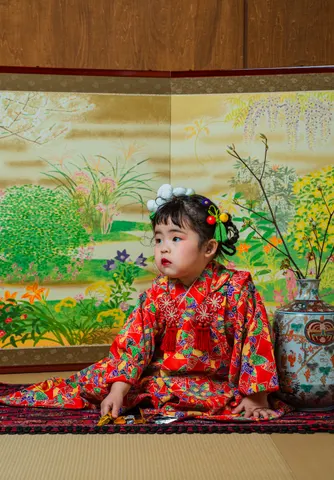 草花の屏風を背景に赤い着物で座る七五三の女の子(Byobu シーン)