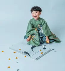 折り紙の本の前で笑う緑の着物姿の七五三の女の子(Orizuru シーン)