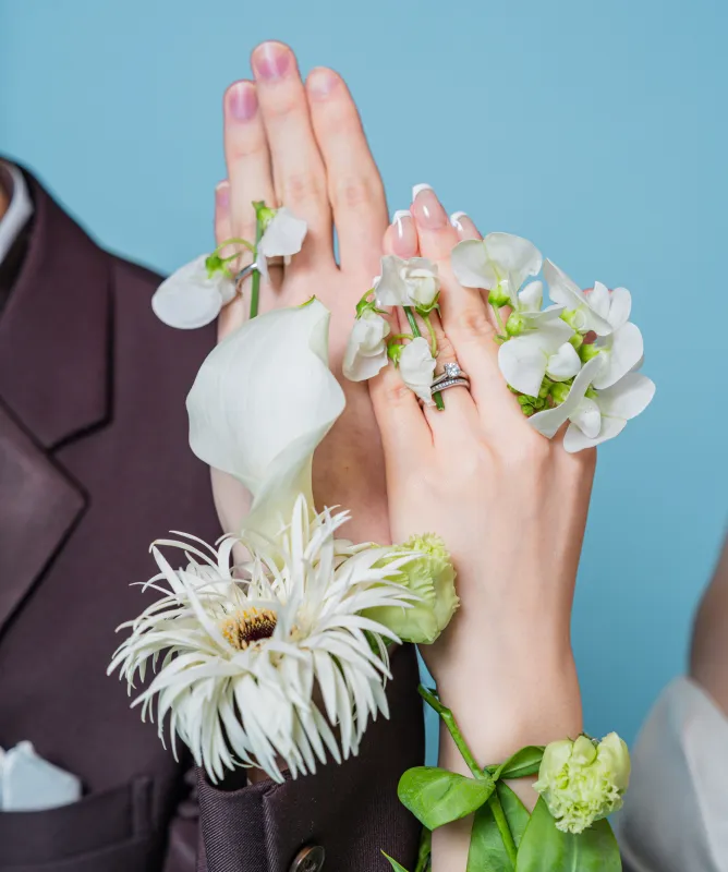 結婚指輪をつけ白い花を添えた新郎新婦の重なる手元(Hands with flowers シーン)