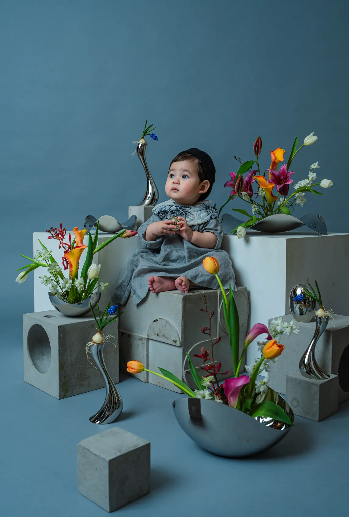 色とりどりの生花と銀の花器に囲まれて積み木に座る赤ちゃん