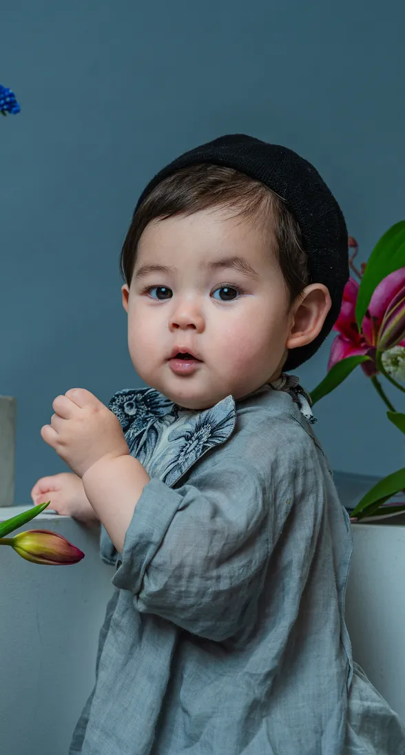 グレーのリネン衣装と黒い帽子を身につけた赤ちゃんのポートレート