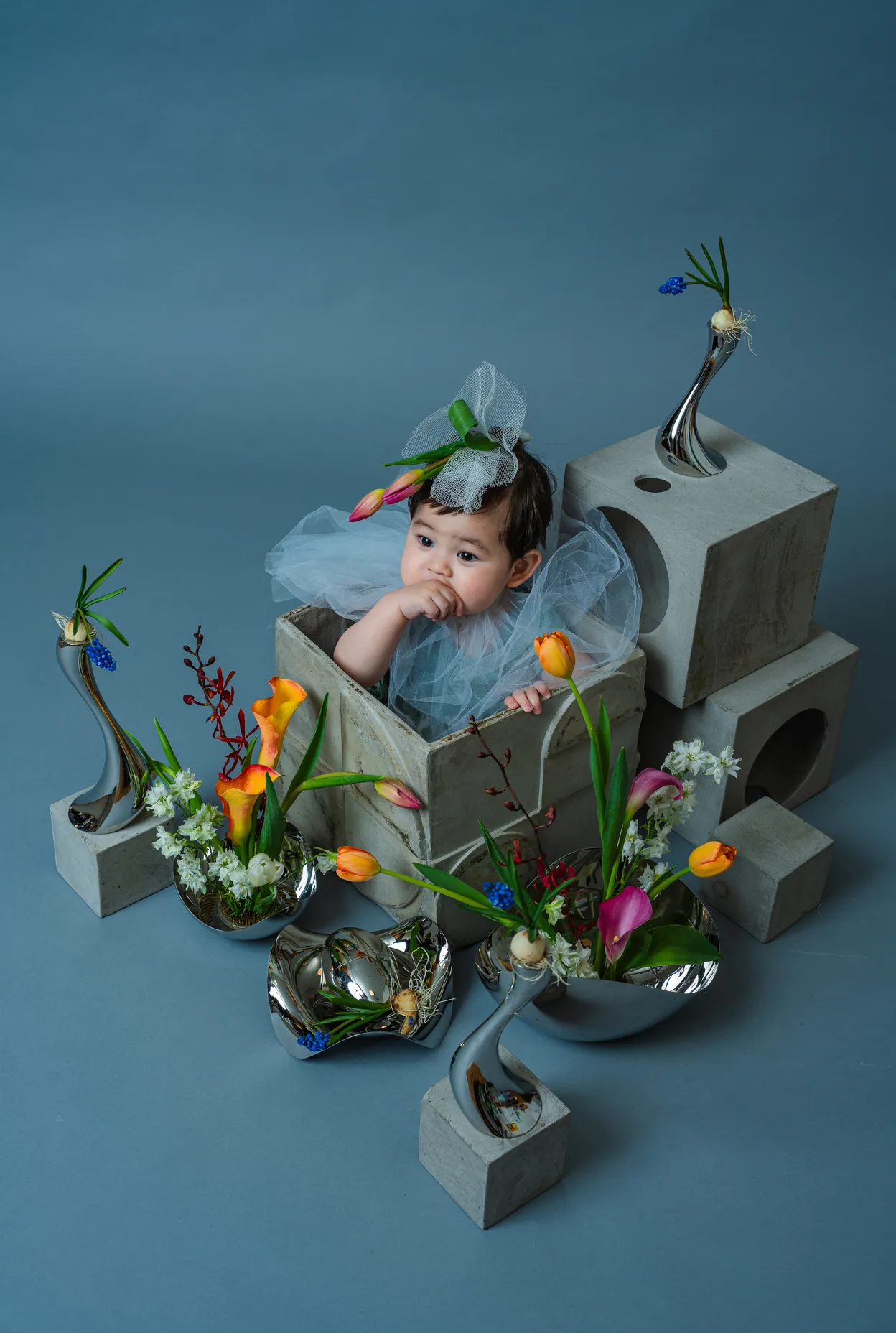チュールをまといコンクリートのオブジェと花に囲まれた赤ちゃん