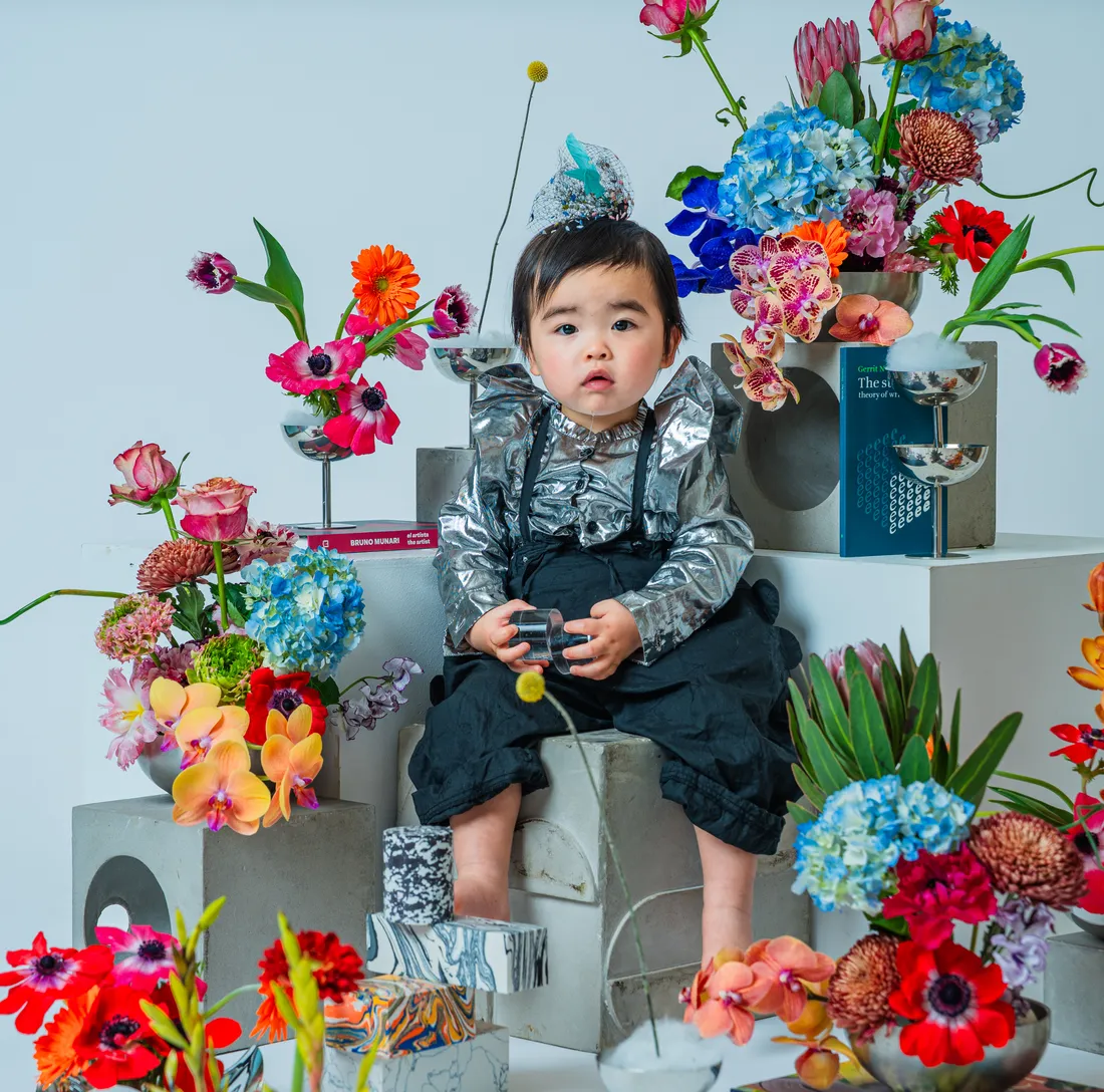 シルバーの衣装で色とりどりの花に囲まれて座る子ども