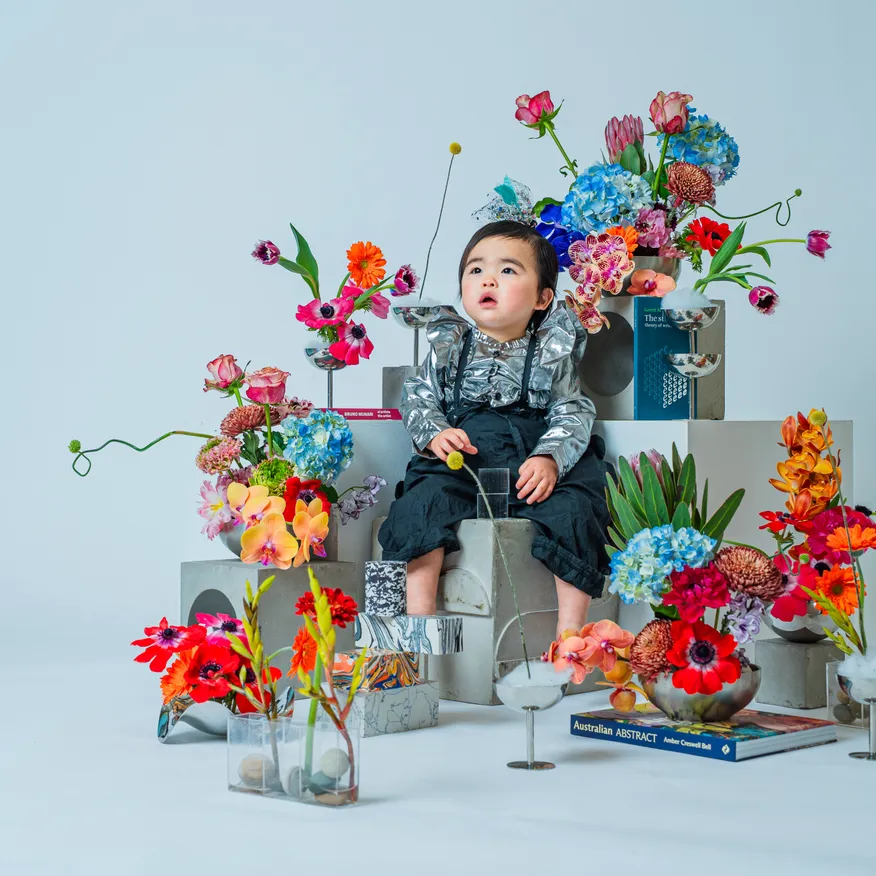 シルバーの衣装で花とオブジェに囲まれ見上げる子どもの全身