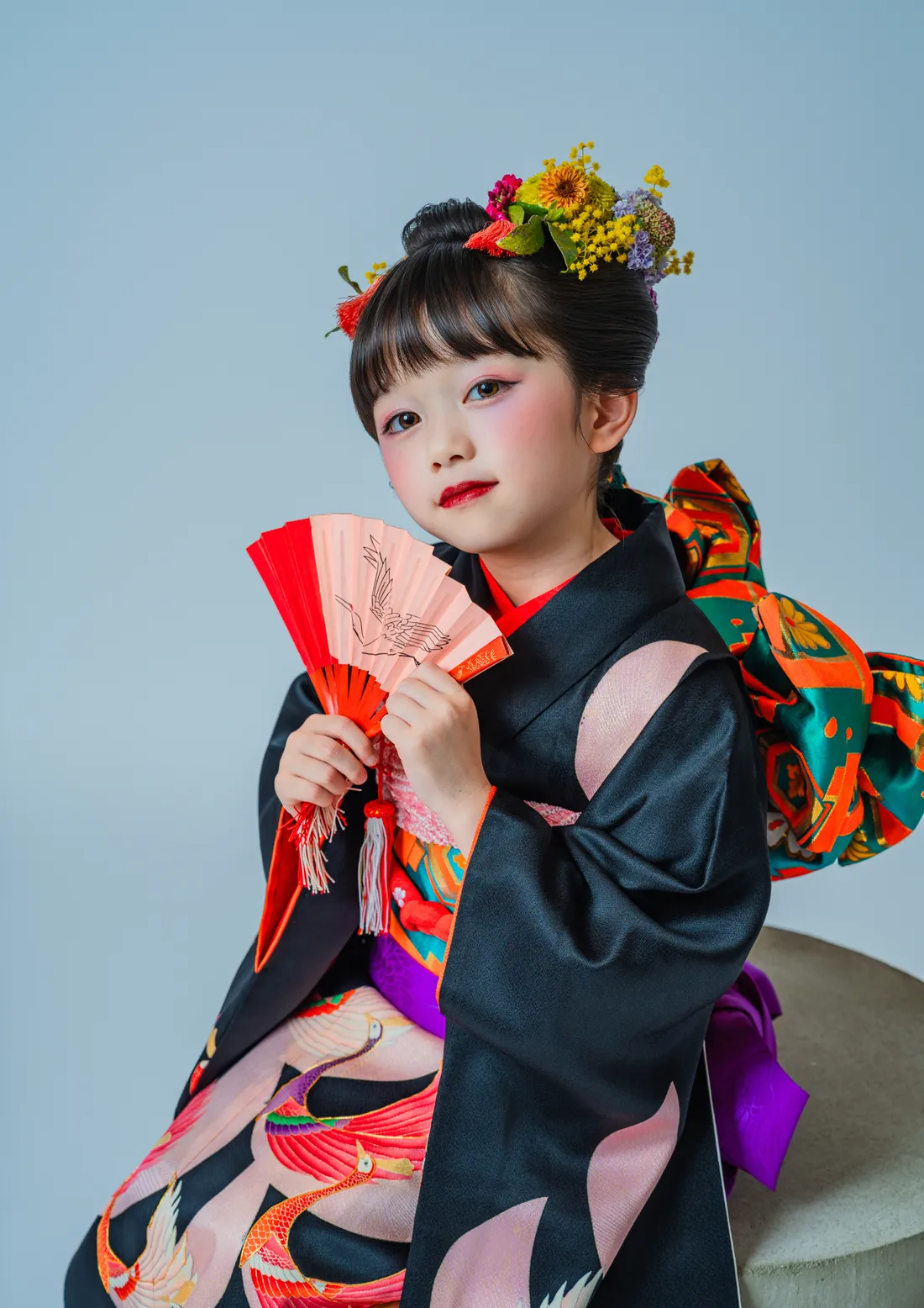 黒い着物に花飾りを付け鶴柄の扇子を持つ七五三の女の子