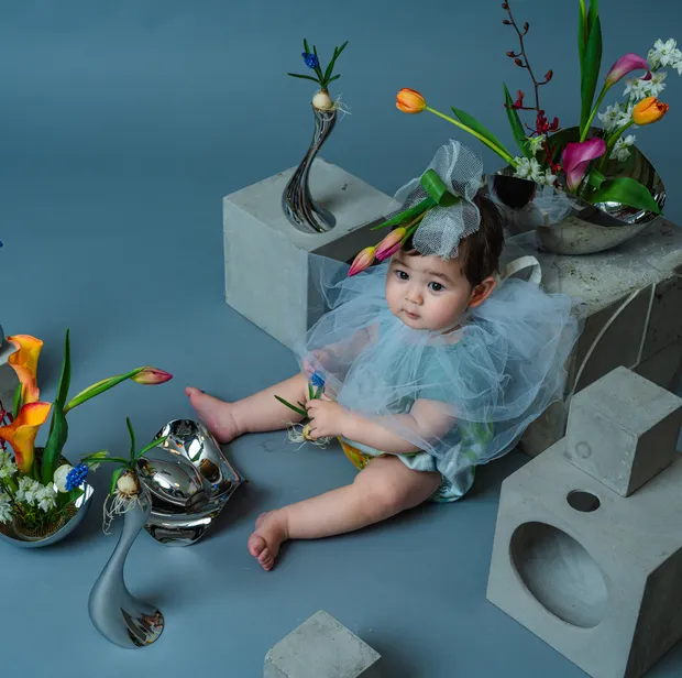 淡い水色のチュールをまとい花を手に座る赤ちゃん（フローラルフォト作品）