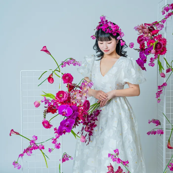 白いドレスと花冠をまといピンクの花に囲まれてうつむく花嫁