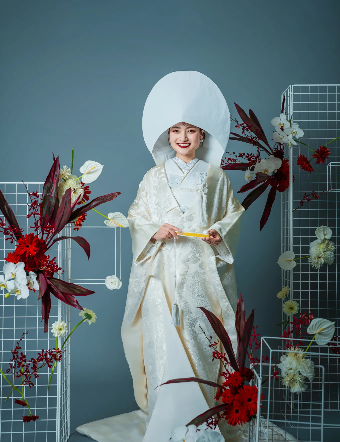 白無垢と綿帽子をまとい扇子を持って微笑む和装の花嫁の全身